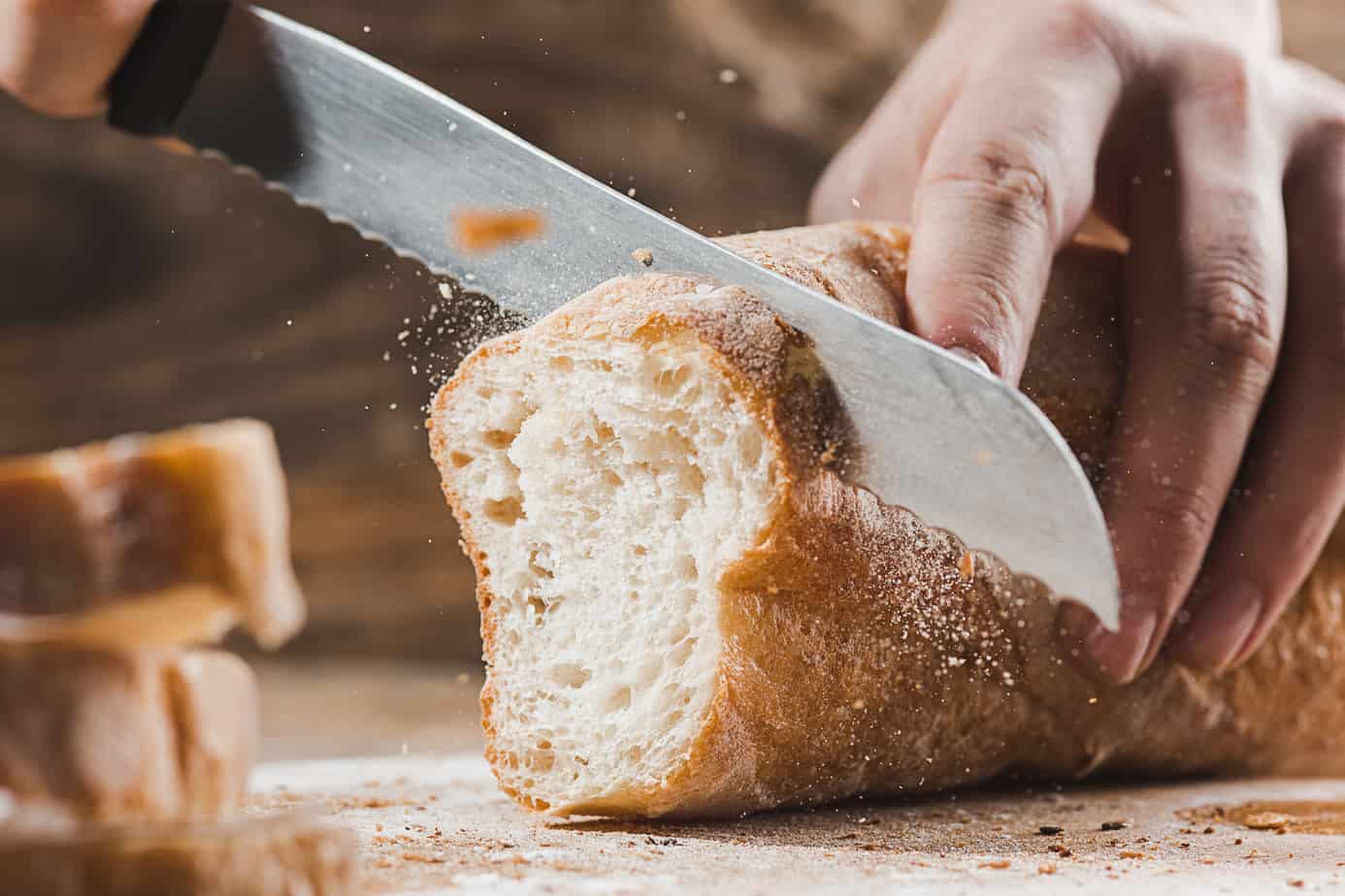 using a bread knife to slice through a crusty baguette