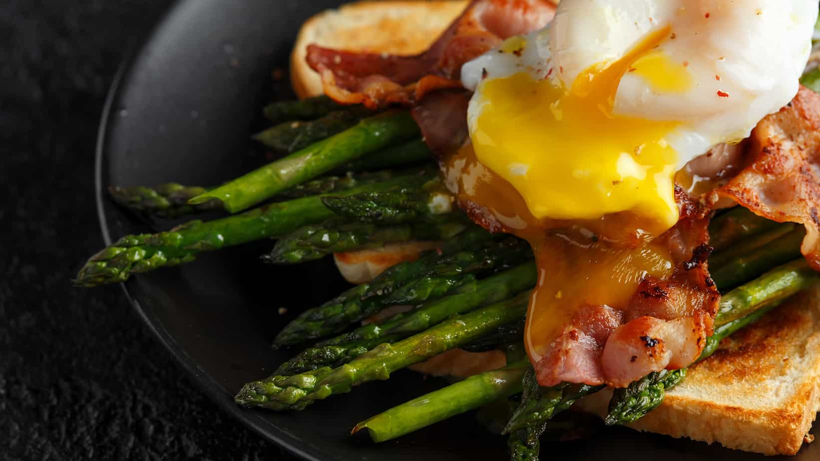 toast topped with asparagus, bacon and a poached egg.