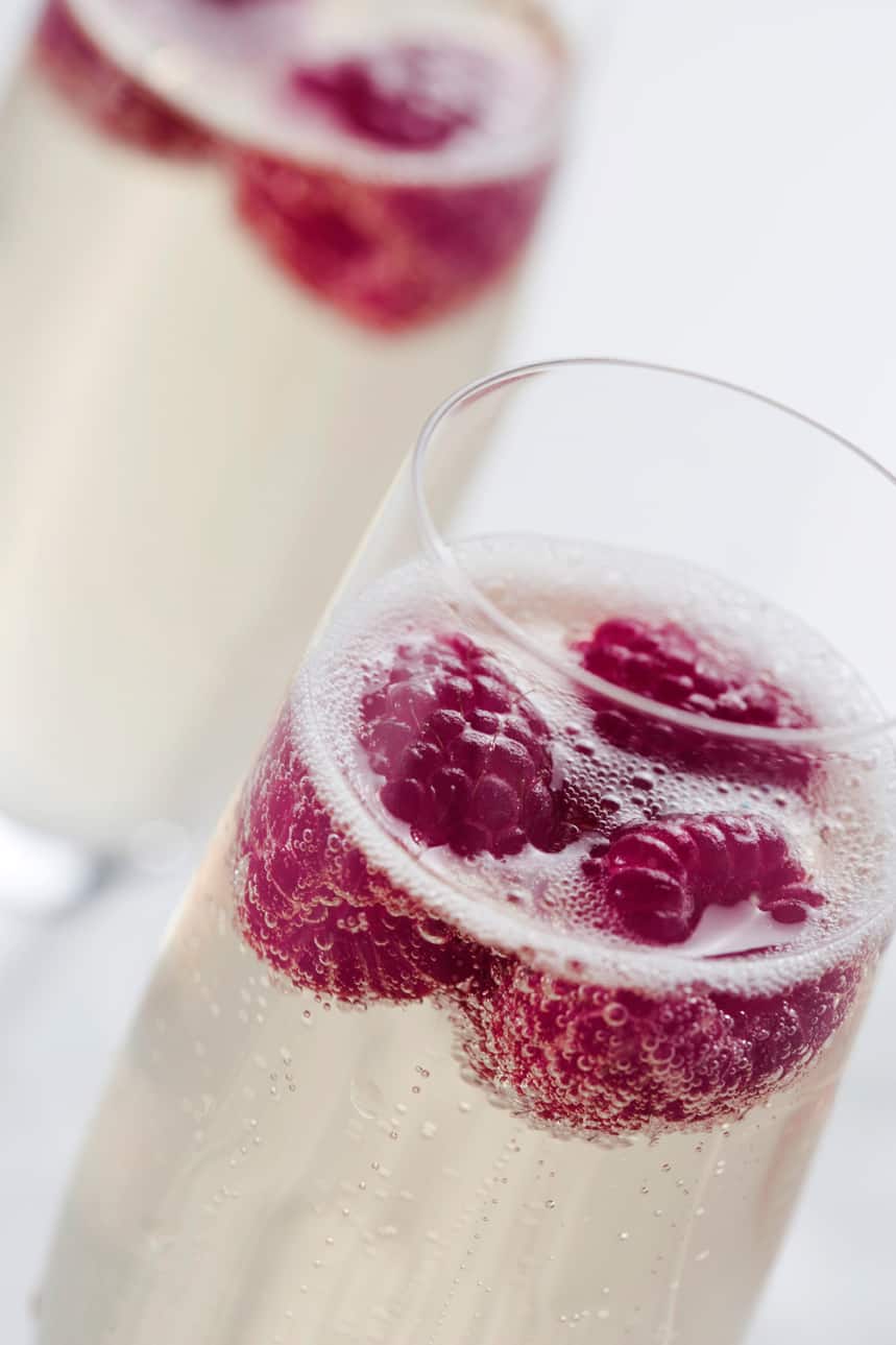 glass of elderflower infused champagne spritz cocktail with 3 raspberries floating in it