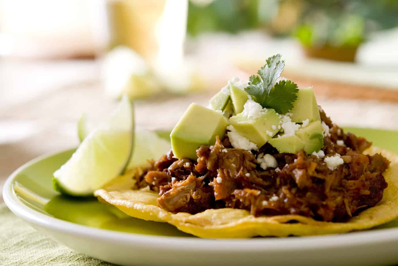 spicy beef tostada topped with guacamole and cilantro with cotija cheese