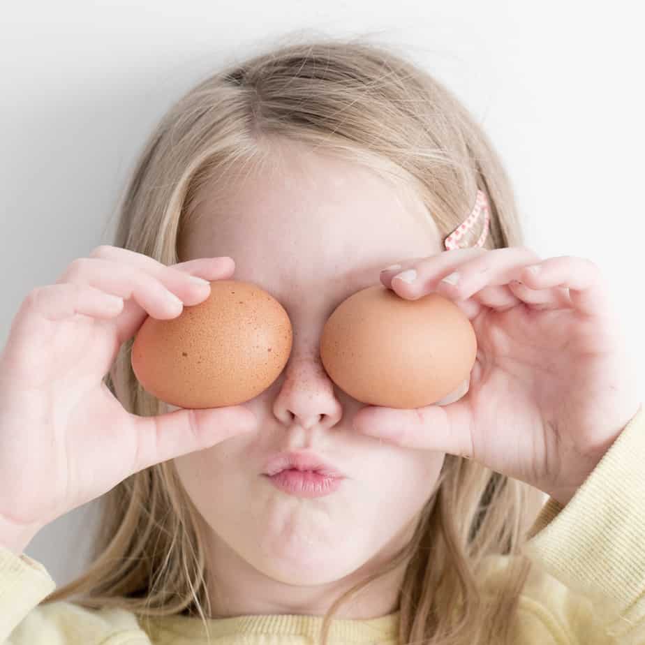 Little girl holding eggs up in front of her eyes.