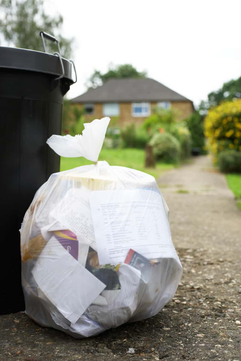 un coș de gunoi cu o pungă de plastic transparentă de gunoi pe pământ lângă el.