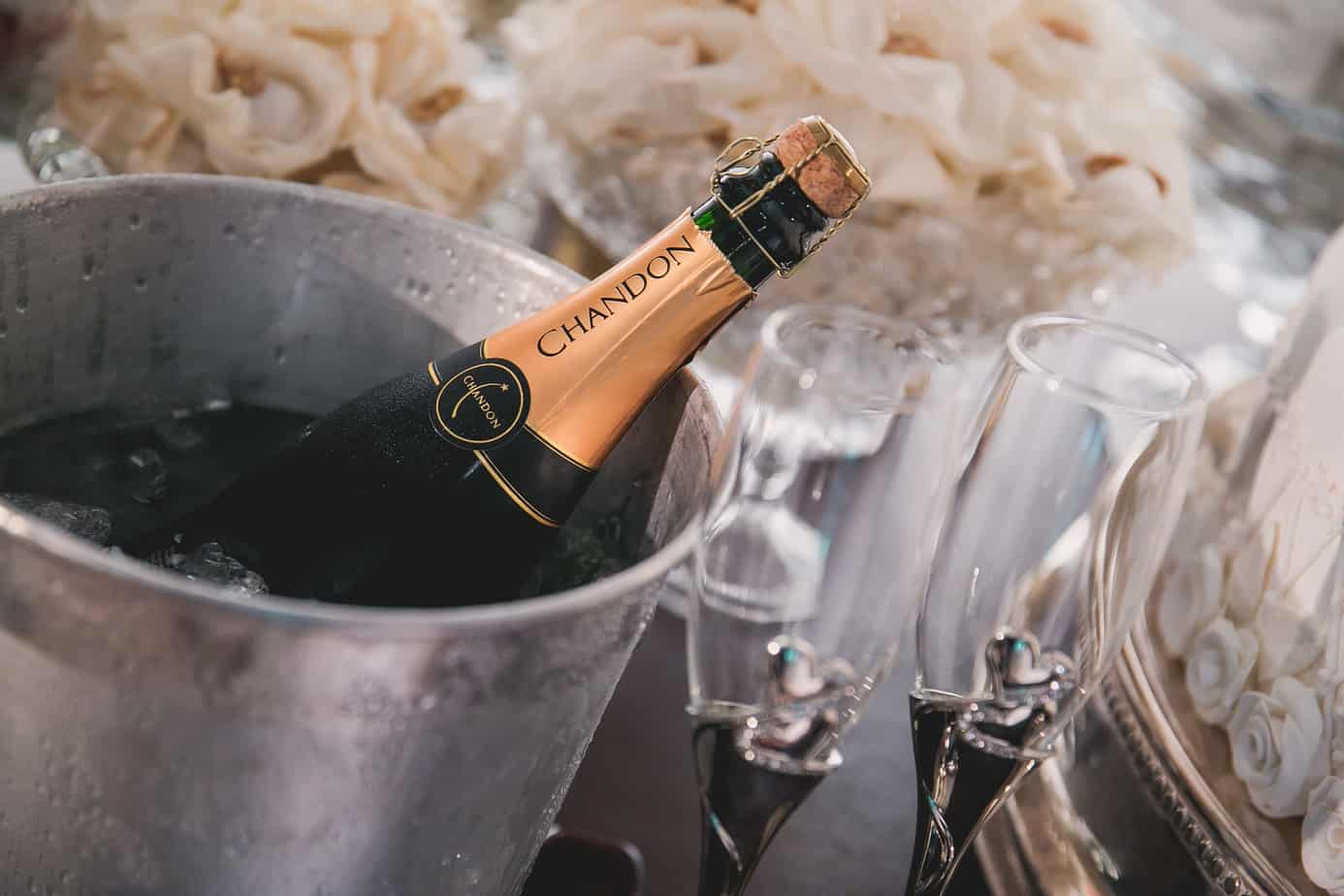 a bottle of chandon champagne in an ice bucket with two fancy champagne flutes next to it.