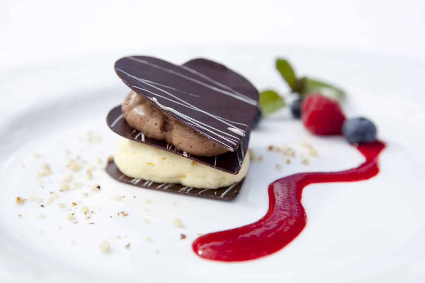 layered chocolate confection featuring dark chocolate, vanilla mousse, milk chocolate mousse, and raspberry coulis