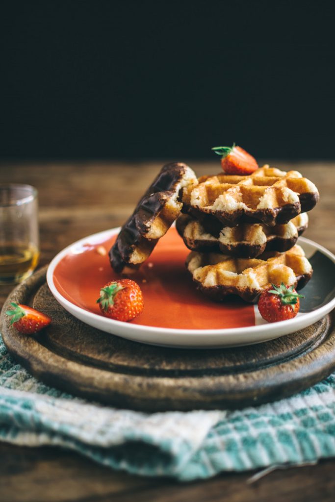 Mini belgian waffles with bottoms dipped in chocolate, accompanied by berries.