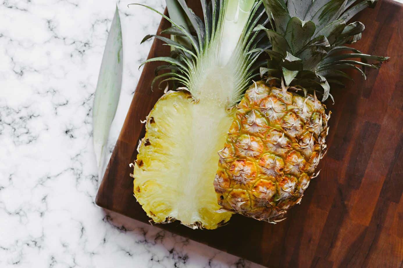 A perfectly ripe pineapple sliced open top to bottom, placed on a wooden cutting board.