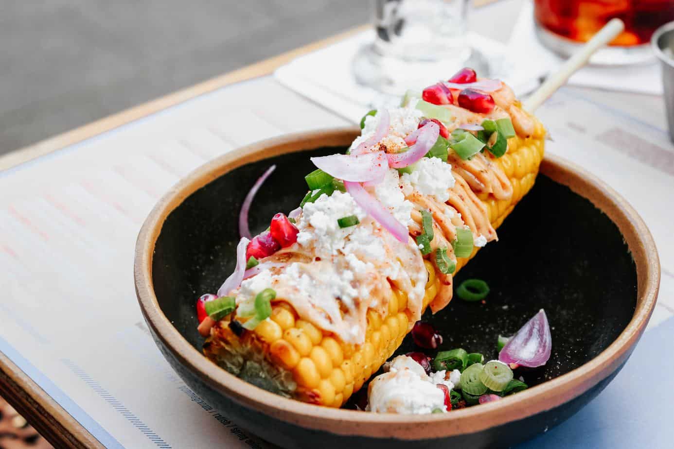 grilled mexican elotes corn on a skewer in a black ceramic bowl