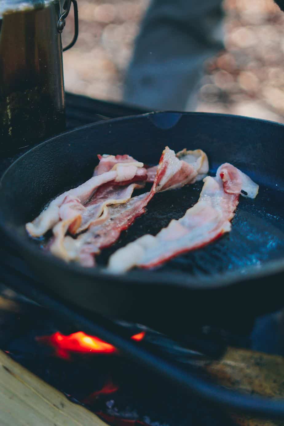 bacon cooking in a cast iron pan over a wood fire