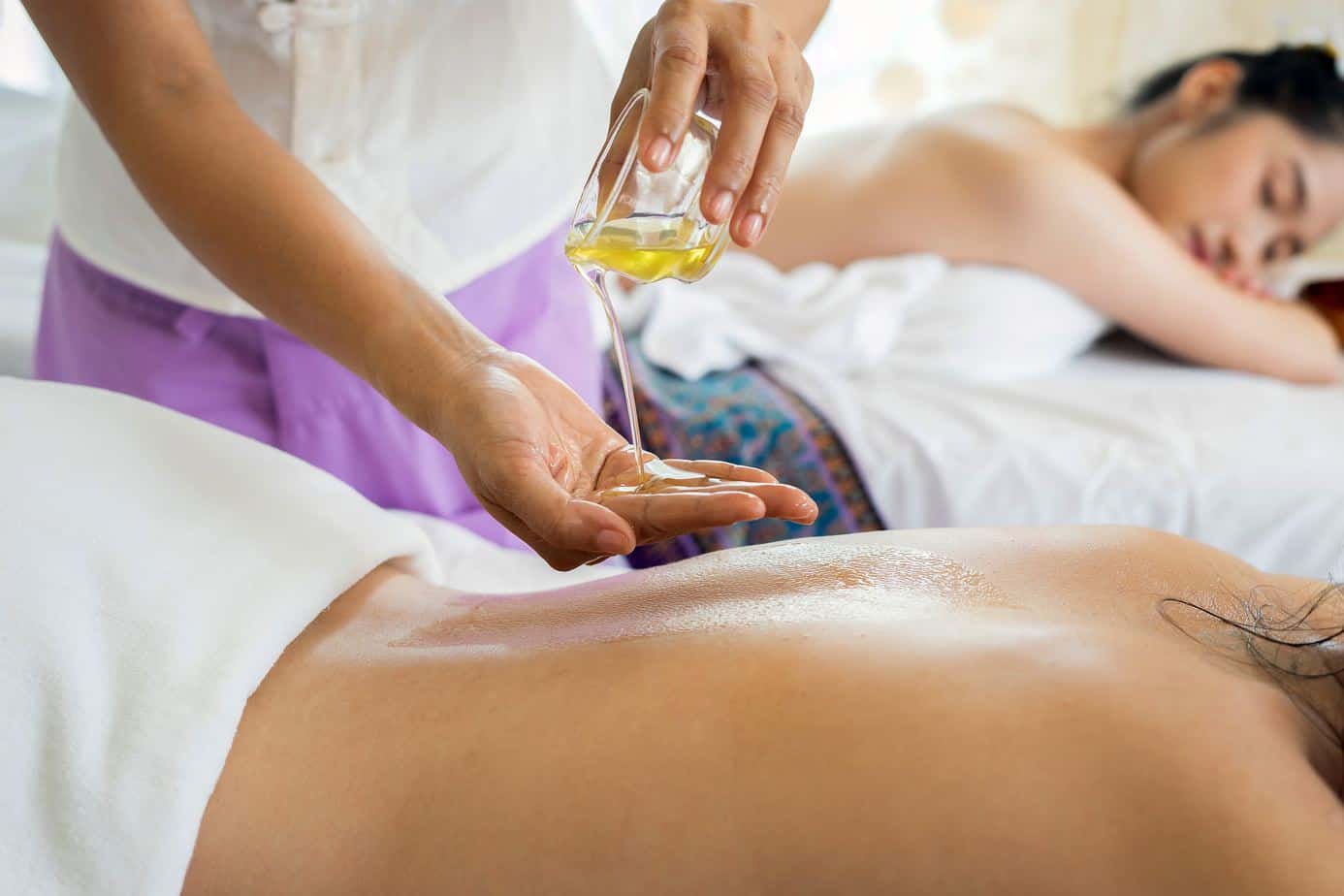 massage therapy, two women pictured, one with hot oil being poured into her hand.