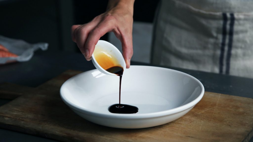 worcershire sauce being poured from a white ramekin into a larger white bowl.